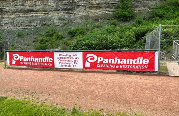 Panhandle Cleaning and Restoration company logo on a banner at a local little league baseball field.