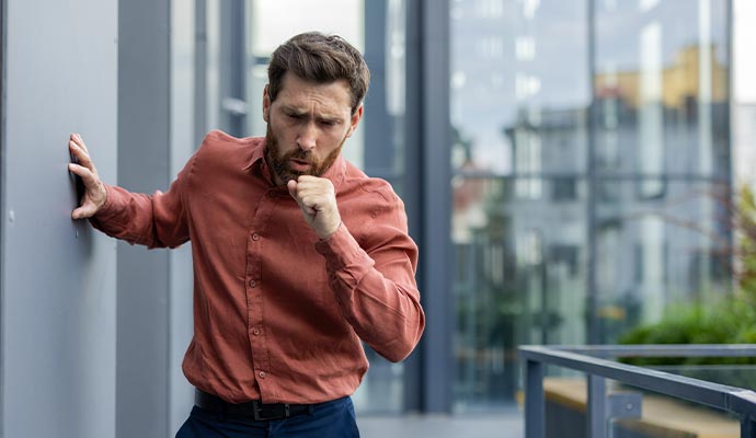 Man experiencing coughing outdoors Man coughing while standing outside a building