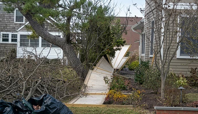 Fallen tree on broken wooden fence with debris bags