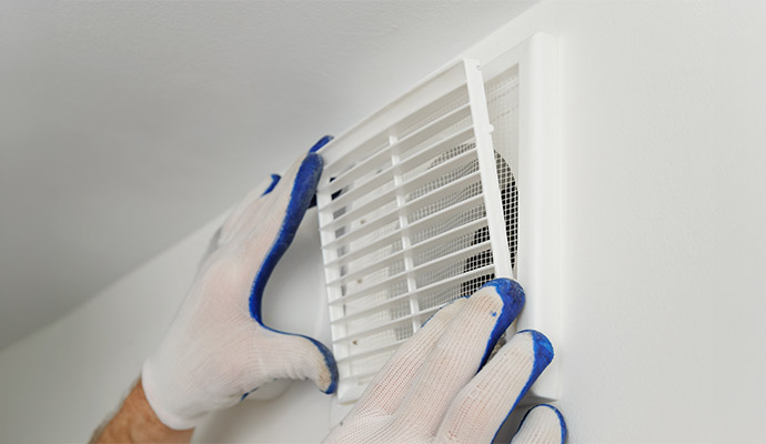 A person installing a white ventilation grille onto a wall