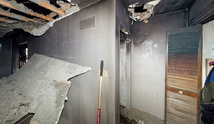 Fire-damaged room with a collapsed ceiling, exposed framing, and soot-covered walls