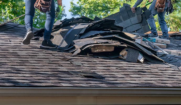 Roofing contractors replacing damaged asphalt shingles on a residential roof after a hailstorm