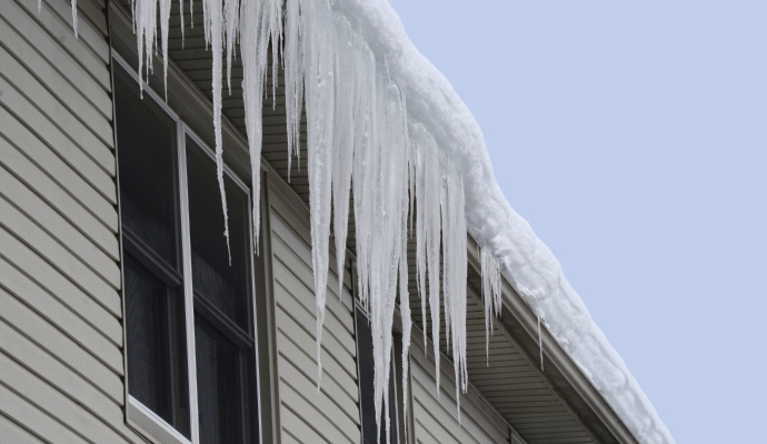 Large icicles hanging from a snow-covered residential roof edge and gutter