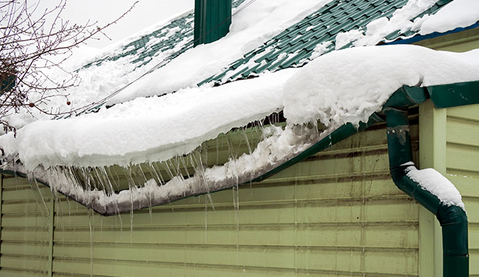 Metal roof gutter bent and sagging under heavy snow accumulation and icicles