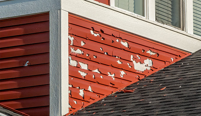 Vinyl siding punctured and cracked by severe hail impact near the roofline