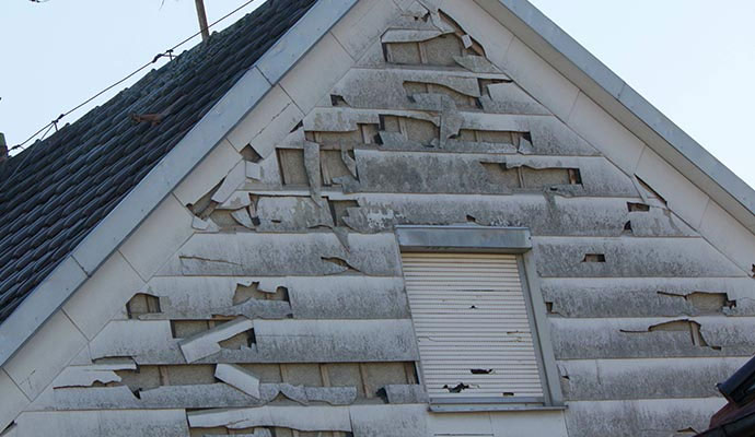 Residential house exterior wall with shattered and peeling siding panels from hail impact