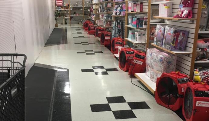 Row of industrial air movers drying a commercial store floor.
