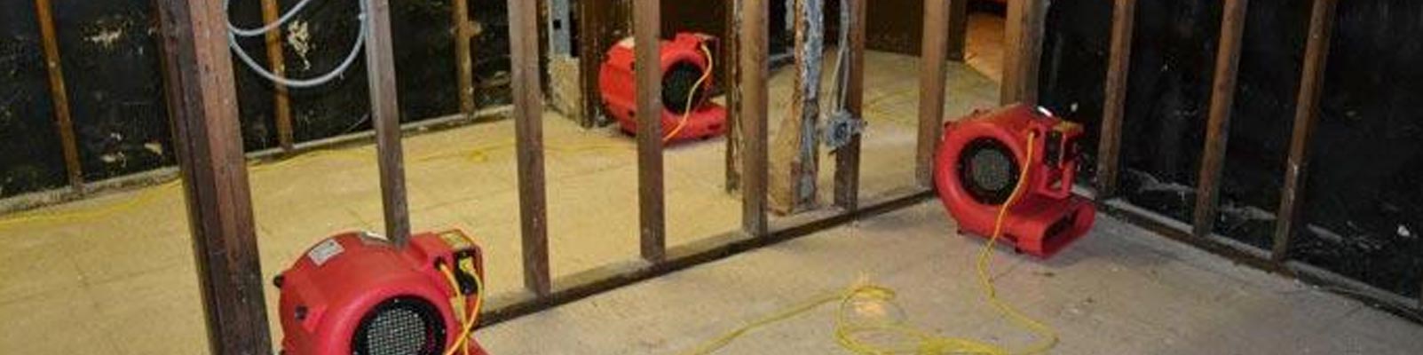 Industrial air movers drying a flooded room's framework.