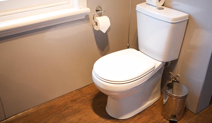 White Toilet on Wood Bathroom Floor with Chrome Bin